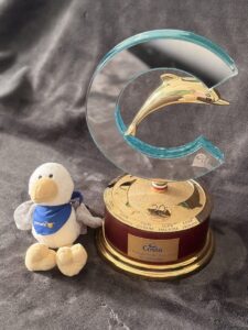 Costa-Trophäe I Protagonisti del Mare 2012 mit der Gravur N°1 Germany, daneben ein Plüschvogel mit Pomorin-Halstuch